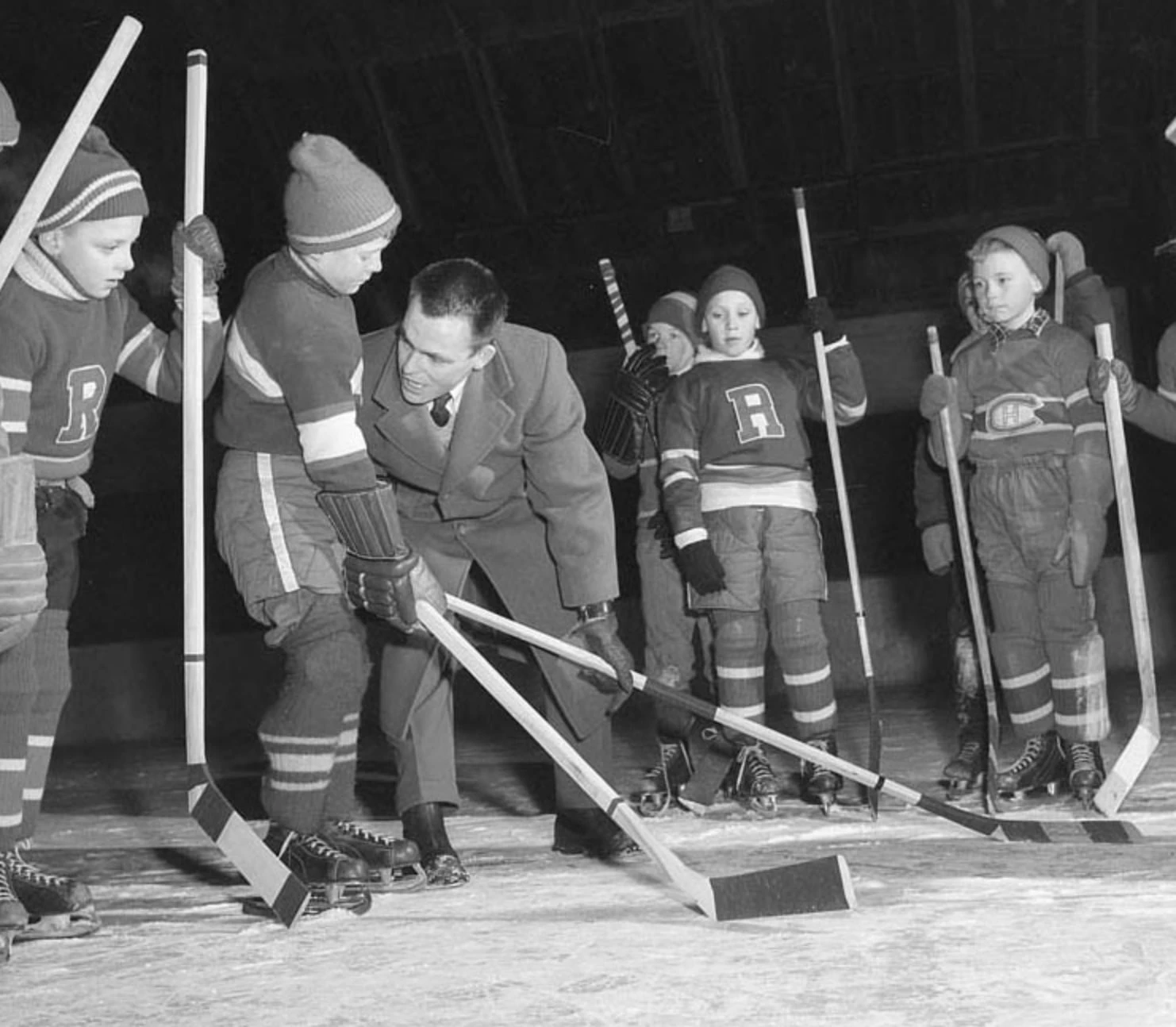A coach helps children position their hockey sticks on the ice.
